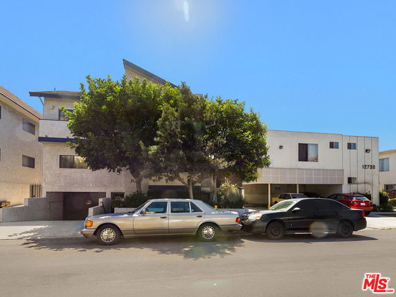 Front view of a multi-story building with modern design elements, adjacent to parked cars on the street.
