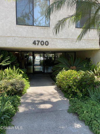 Entrance of a building with foliage around the walkway and glass doors.