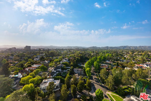 Panoramic view of a residential area with houses and trees, extending towards distant hills.