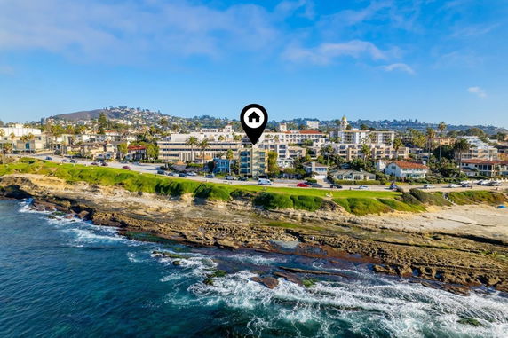 Coastal view of buildings along a rocky shoreline with waves crashing onto the rocks.