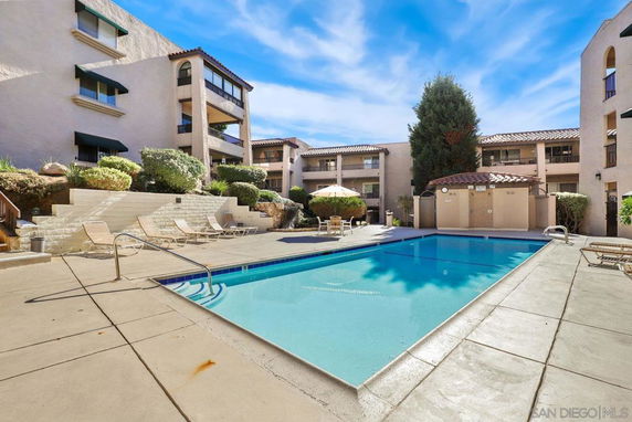 Outdoor swimming pool area with sun loungers and surrounding multi-story buildings.