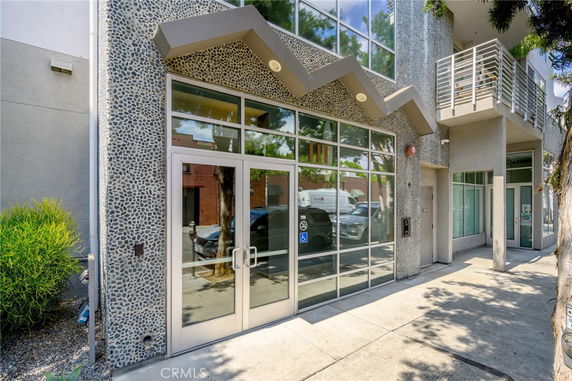 Front view of a modern building with large glass doors and windows, featuring a pebble-textured facade and balcony.