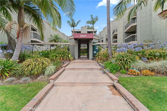Front view of a multi-story apartment building with balconies and a gated entrance.