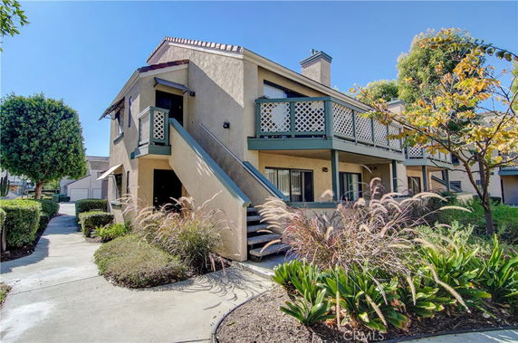 Front view of a two-story residential building with exterior stairs and greenery.