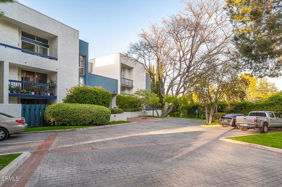 Outdoor parking area with multiple vehicles and a view of a multi-story building with balconies.
