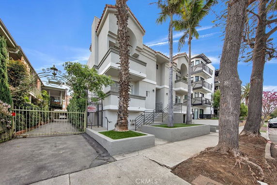 Front view of a multi-story apartment building with balconies and a gated driveway.