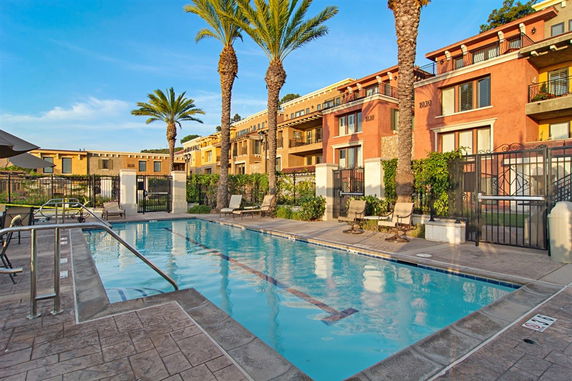 Outdoor swimming pool area with surrounding buildings and palm trees.