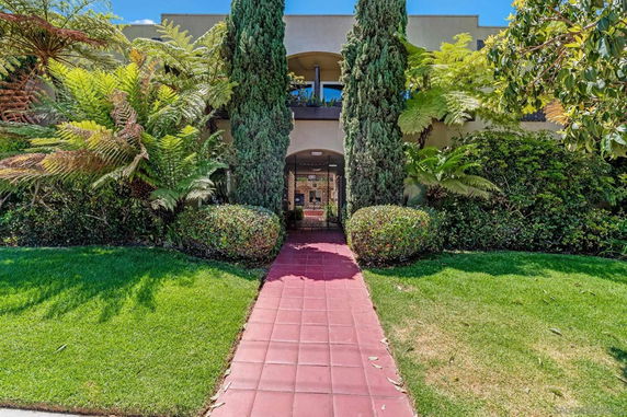 Front view of a building entrance with a pathway and lush greenery.