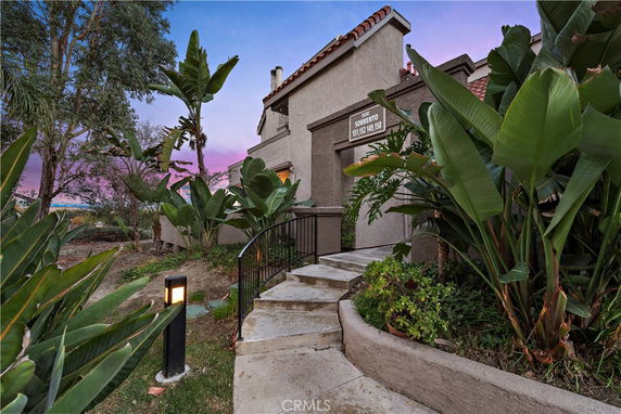 Front view of a multi-story building with a pathway and tropical plants.