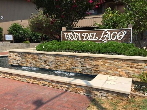 Front view of a building entrance with a sign that reads 'Vista Del Lago' and a decorative stone waterfall feature.