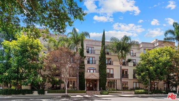 Front view of a multi-story residential building with trees and a walkway.