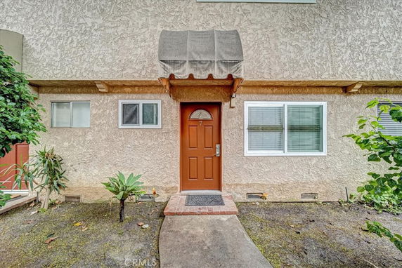 Front view of a house with a red door and light-colored stucco exterior.
