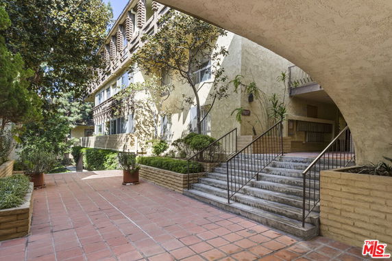 Front view of a multi-story building with stairway entrance and greenery.