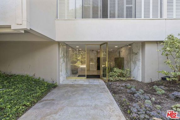 Front view of a building entrance with glass doors and surrounding greenery.