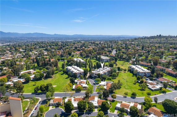 Wide-angle aerial view of a residential area surrounded by greenery and distant mountains.