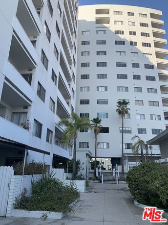 Front view of a multi-story residential building with balconies and palm trees.
