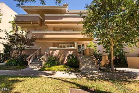 Front view of a multi-story building with balconies and stairs leading to the entrance.