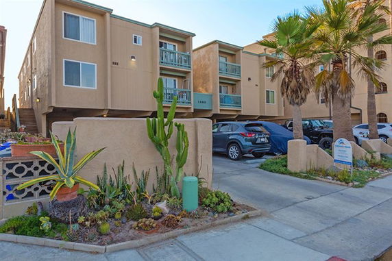 Front view of a multi-story residential building with parking area in front.