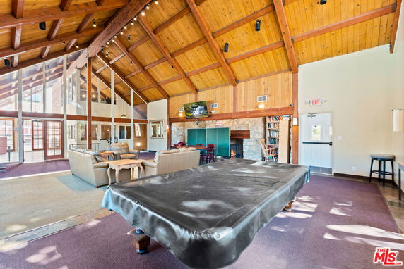 Interior view of a recreation area with vaulted wooden ceiling, large windows, and a billiard table.