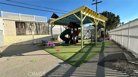 Outdoor play area with a slide and play equipment under a shaded structure.