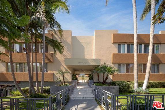 Front view of a multi-story building with a walkway and palm trees.