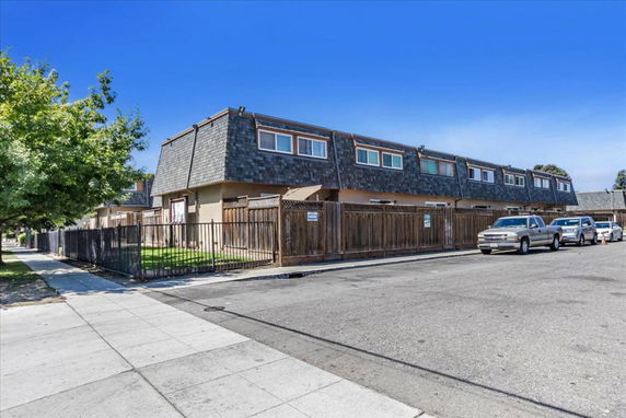 Front view of a two-story building with a fenced area and parked cars on the street.