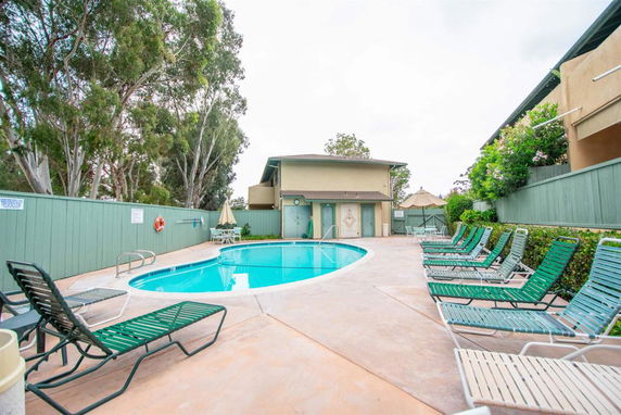 Swimming pool area with surrounding lounge chairs and a building in the background.