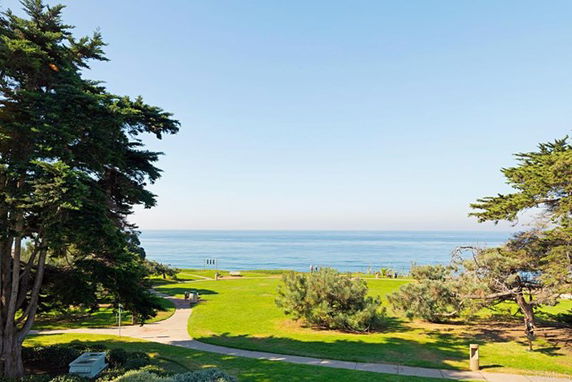 Wide angle view of a park with greenery and a sea in the background.