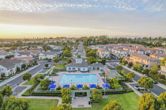 Aerial view of a neighborhood with a central community clubhouse and swimming pool, surrounded by residential homes and streets.