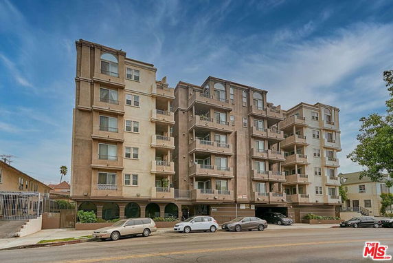 Front view of a multi-story apartment building with balconies and parking at the ground level.
