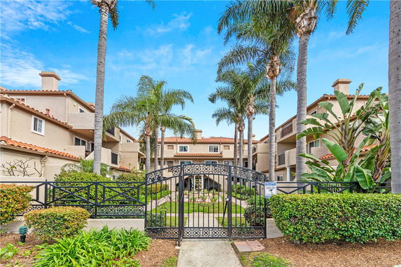 Front view of a multi-story residential building with a gated entrance and palm trees.