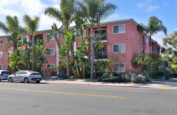 Front view of a three-story apartment building with a pink exterior and multiple balconies.