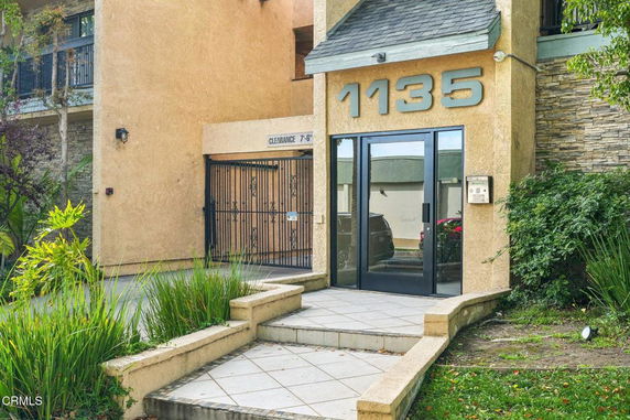 Front view of a building entrance with large numbers and a gated parking entrance.