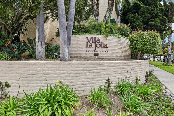 Front view of a condominium sign with surrounding greenery.