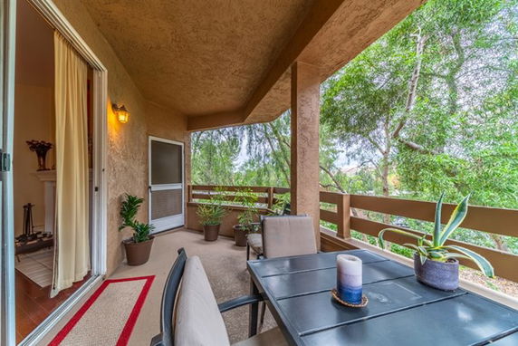 Outdoor patio with table and chairs, surrounded by greenery.