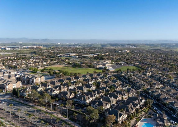 Aerial view of a suburban area with multiple houses and roads, surrounded by open land and distant hills.