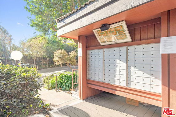 A row of mailboxes integrated into an outdoor structure surrounded by trees and shrubs.