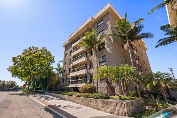 Front view of a multi-story apartment building with balconies and palm trees.