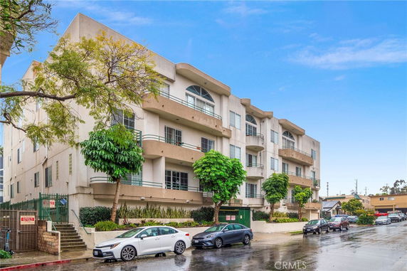 Front view of a multi-story residential building with balconies and trees in front.