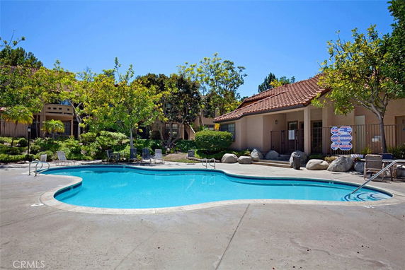 Outdoor swimming pool with surrounding patio area and nearby building in the background.