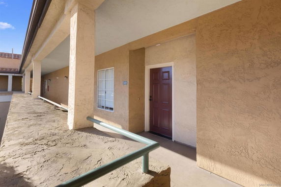 Exterior view of a building corridor with beige walls and a row of doors.