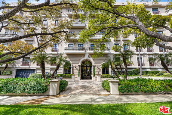 Front view of a multi-story residential building with balconies and landscaped entrance.
