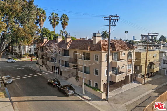 Front view of a multi-story apartment building with balconies and a tiled roof.