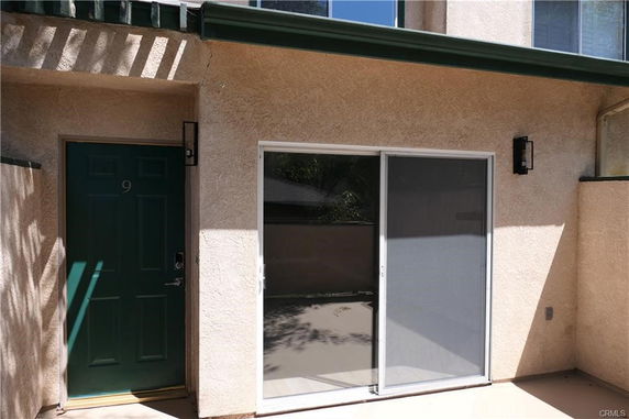 Front view of a residential building entrance with a green door and sliding glass door.