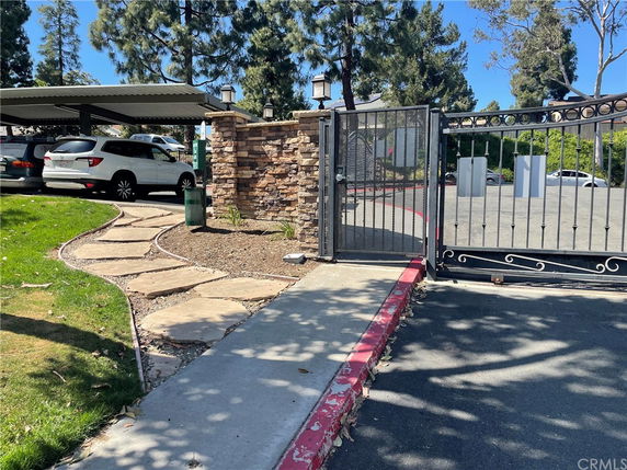 Outdoor view showing a gated entrance with a covered parking area and stone pathway.