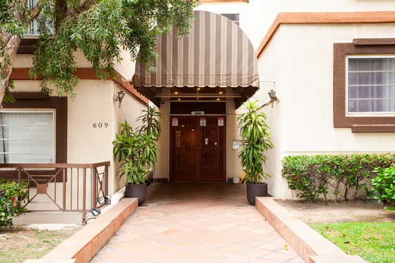 Front view of a building entrance with a striped awning and potted plants.