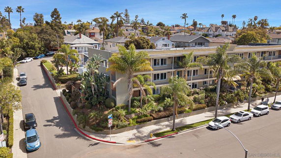 Front view of a three-story residential building with balconies and palm trees in front.