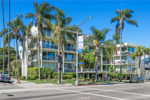 Front view of a multi-story apartment building with balconies and palm trees.
