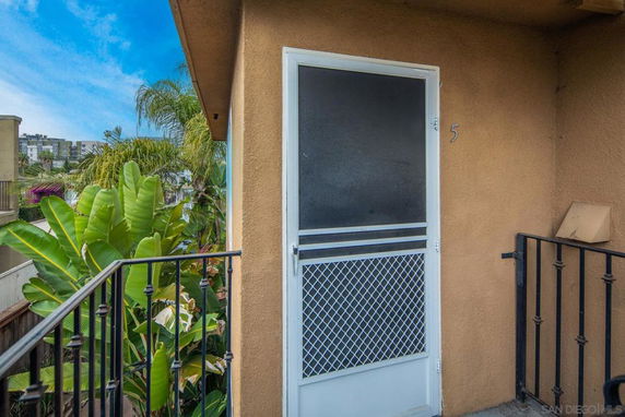 Entrance to an apartment with a screen door, railing, and surrounding greenery.