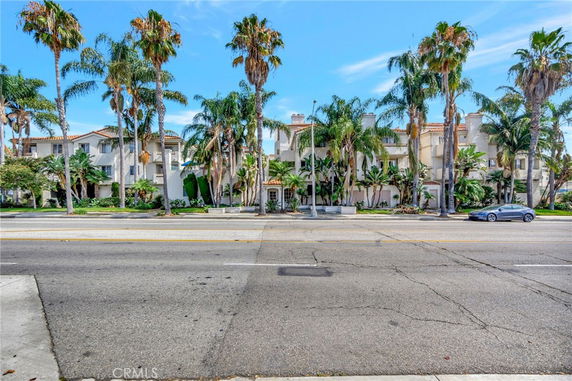 Front view of a multi-story residential building with palm trees lining the street.